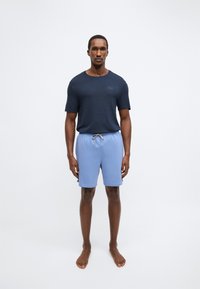 T-shirt texturizada de manga curta azul-marinho e calções com cordão em azul claro. Os calções apresentam um tecido macio e um corte até ao joelho. Sem calçado.