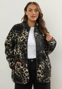 Futro sztuczne w czarno-beżowy wzór w panterę, z zamkiem z przodu, czarną kieszenią i kontrastowym wykończeniem. Miękka, teksturowana tkanina.