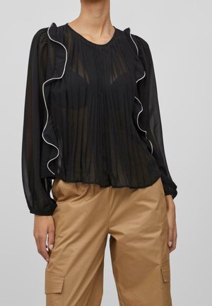 Czarna przezroczysta bluzka z pionowymi zakładkami, falbankowymi krawędziami i białym obszyciem wzdłuż dekoltu. Długie rękawy z elastycznymi mankietami.