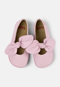 Zapatos de cuero rosa con puntera redondeada y un gran lazo anudado en la parte delantera. En el interior cuentan con una plantilla beige en contraste con texto rojo.