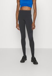 Leggings noirs avec une texture lisse, taille haute et design ajusté. Associés à un brassière de sport bleu courte et des chaussures de sport noires.