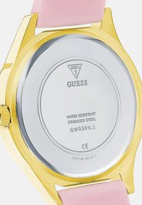 Kullatud kuldse tooni Guess käekella tagakülg, millel on roosat värvi rihm, näitab logo, veekindel roostevaba teras, mudel GW0381L2 ja Jaapani töömehanism.