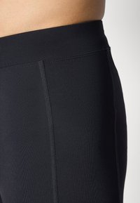 Fekete leggings magas derékkal, sima, rugalmas anyagból, finom varrási részletekkel az oldalán.