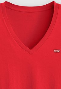 Red cotton v-neck t-shirt featuring a ribbed neckline and a small white Levi's logo patch on the left side. Soft, smooth texture.