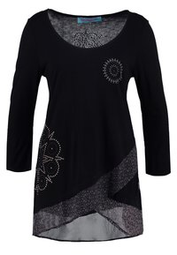 Svart långärmad tunika med rundad halsringning, prydd med silverfärgade nitar och en mönstrad genomskinlig nederdel. Mjuk, lättvikts tyg.