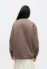 Καφέ φαρδιά φούτερ με κατεβασμένους ώμους και στρογγυλή λαιμόκοψη, κατασκευασμένο από απαλό ύφασμα. Διαθέτει ριμπ μανσέτες και τελείωμα.