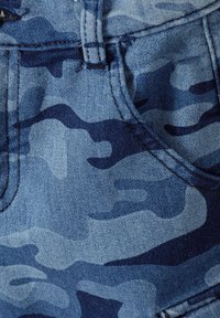 Bermuda in denim blu con un motivo camouflage in diverse sfumature di blu. Presenta tasche cucite e una cintura. La texture è liscia.