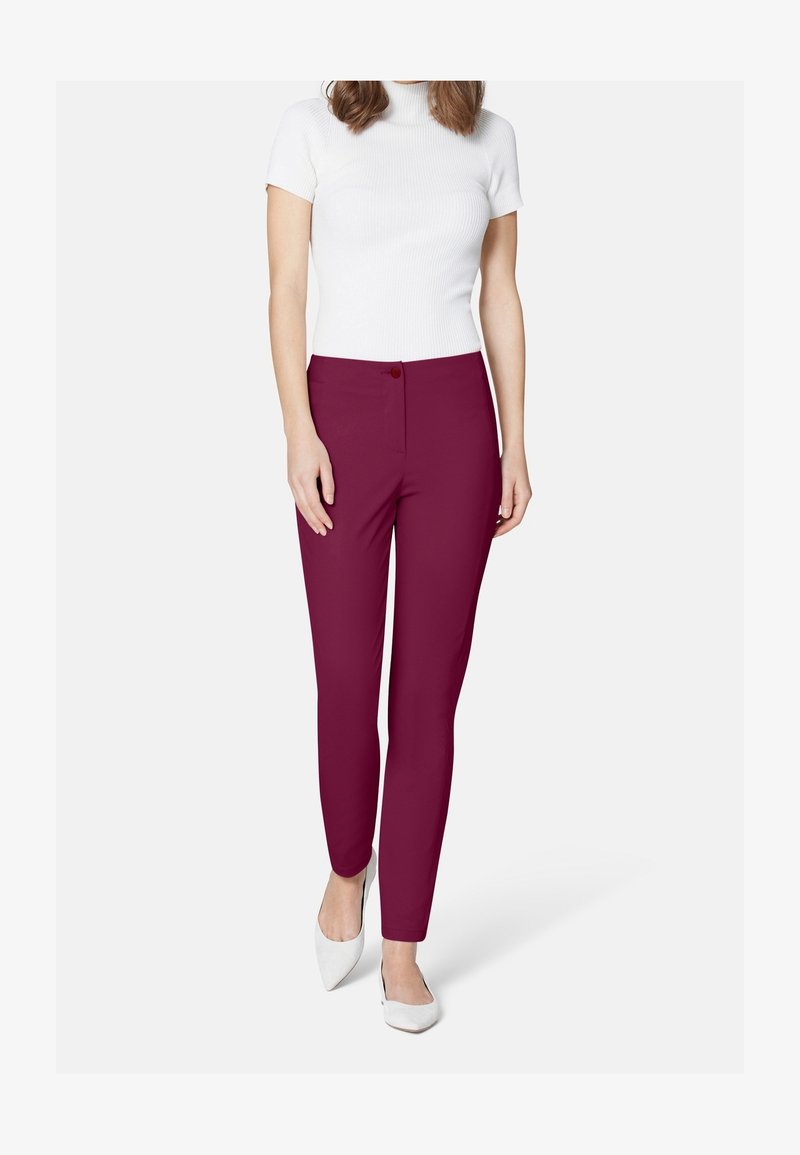 Pantalon slim bordeaux avec fermeture à boutons, confectionné dans un tissu lisse. Associé à un haut blanc côtelé à manches courtes et des talons blancs.