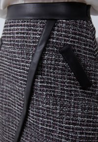 Tweedová sukňa s textúrovaným čierno-bielo-fialovým vzorom; obsahuje čierne kožené akcenty a elegantný pás.