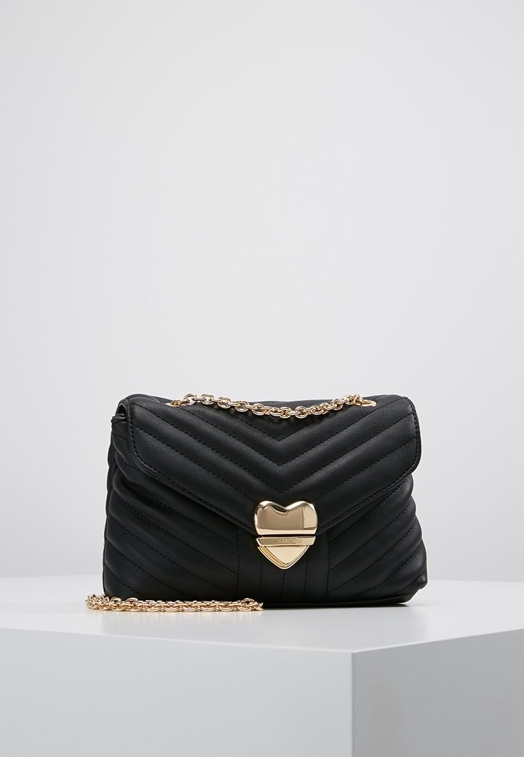 Svart kviltad handväska med zigzag-mönster, gyllene kedjerem och hjärtformad lås. Tillverkad av syntetiskt material med en slät textur.