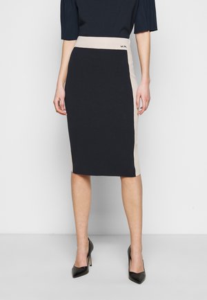 Kokerrok tot op de knie in marineblauw en beige, met een aansluitende pasvorm, geribbelde tailleband en een gladde textuur. Zwarte hoge hakken.