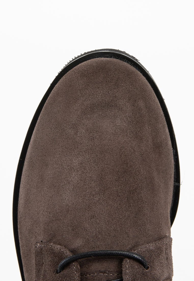 Chaussure en daim marron avec une texture lisse, dotée d'un bout arrondi, de lacets noirs et d'une semelle noire contrastante. Design simple et lignes épurées.