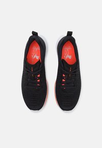 Par de zapatillas de running negras de punto con plantillas naranjas, cordones negros y suelas blancas, vistas desde arriba sobre un fondo blanco.