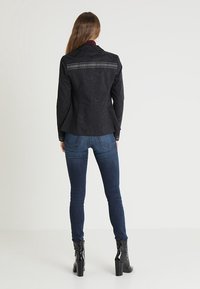 Czarna żakiet o teksturowanej powierzchni z srebrnymi paskami na ramionach, w połączeniu z ciemnoniebieskimi skinny jeansami i czarnymi botkami na obcasie.