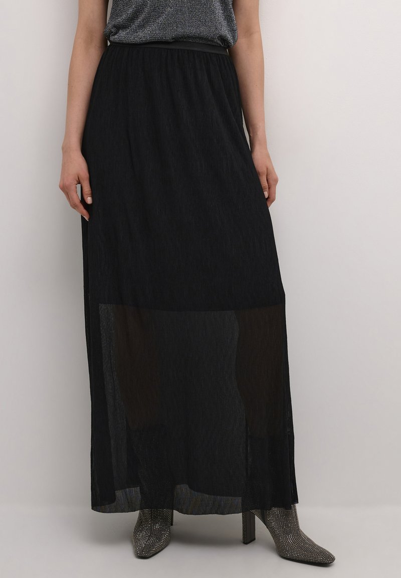 Schwarzer Maxikleid mit fließendem Design, ausgestattet mit transparenten Einsätzen am unteren Ende und einem elastischen Bund. Kombiniert mit metallischen High-Heel-Stiefeln.