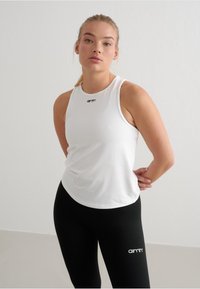 Top senza maniche bianco con scollatura rotonda e logo nero; abbinato a leggings neri con un logo bianco sulla gamba. Tessuto morbido.