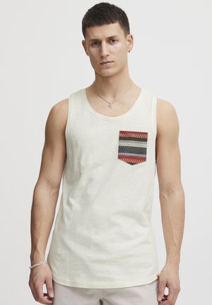 Lichtbeige tanktop van katoen, met een geprinte patchzak in rood, groen en blauw zigzagpatroon op de linkerkant van de borst.