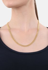 Collana di catena dorata con anelli intrecciati indossata attorno al collo sopra una maglia nera su una persona con lunghi capelli raccolti.