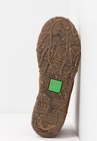 Gumová podrážka obuvi s texturovaným vzorem obsahujícím drážky a výstupky, včetně zelené žabky na čtvercovém akcentu.