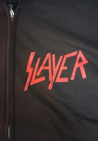 Felpa nera con zip che presenta audaci lettere rosse "SLAYER" in un carattere stilizzato e angolare. Tessuto morbido con una consistenza liscia; design casual.