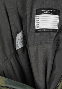 Grå fleece-indvendig med et stofmærke, der beskriver personlige informationer. Med en grøn camo-detalje og lynlås-lukning.