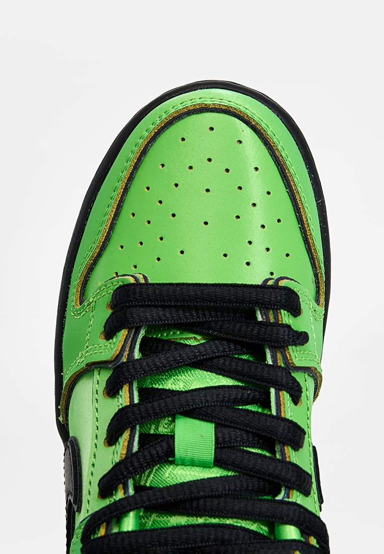 Zapatilla de cuero verde con puntera perforada, cordones negros y costuras amarillas en contraste. Cuenta con un collar acolchado y un logo lateral.