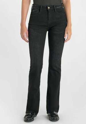 Zwarte flared jeans van denim, met een hoge taille, vijf zakken en subtiele textuur. Het model draagt zwarte schoenen met details.