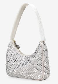 Bolso beige con tachuelas plateadas, material suave, forma curva y una correa de hombro de tela blanca. Cierre de cremallera con un acento metálico.