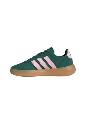 Grüner Sneaker mit pinken Streifen und Absatzdetail, brauner Gummisohle und Schnürdesign.
