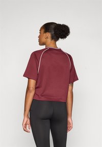 Burgundy cropped t-shirt with short sleeves, white stitching accents, and a round neckline, paired with black leggings.