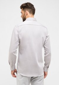 Lichtgrijze langemouwen shirt met een gestructureerde afwerking, voorzien van een klassieke kraag, knoopmanchetten en een gebogen zoom, gezien van de achterkant.