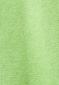 Gros plan sur un tissu tricoté doux de couleur vert clair montrant un motif de points serrés et uniformes ainsi qu'une texture lisse.