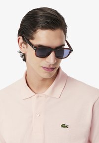 Sköldpaddsmönstrade solglasögon med mörka linser, silverdetaljer på bågarna, tillsammans med en ljusrosa polo offent med en grön logotyp av en krokodil.