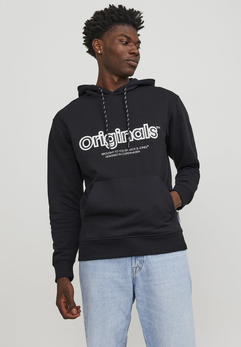 Sudadera con capucha negra y logo blanco "originals", detalles con cordones y un bolsillo frontal. Combinada con jeans de color azul claro. Corte relajado.