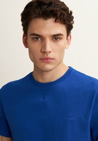 T-shirt in cotone blu con collarino a girocollo e maniche corte, presenta un logo discreto sul petto e una texture liscia.