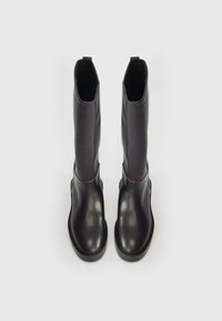 Egy pár magas, fekete bőrcipő, lekerekített orral és vastag talppal, egyenesen állva egy sima fehér háttér előtt.