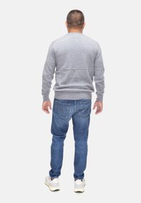 Maglione grigio con polsini e orlo a costine, abbinato a jeans blu con due tasche posteriori e cuciture arancioni. Sneakers bianche completano l'outfit.