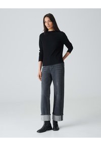 Schwarzer strukturierter Pullover mit langen Ärmeln, kombiniert mit hochtaillierten, weiten grauen Jeans mit umgeschlagenen Säumen, abgerundet mit schwarzen Stiefeletten.