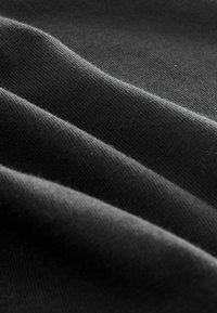 Közelkép puha, sötét szöveten, amelyen látható a finom kötés textúrája és a lágy redők árnyalatváltozásokat hoznak létre.