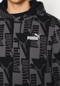 Sweat à capuche noir et gris avec des motifs géométriques, arborant le logo Puma en blanc. Le matériau est doux, et la texture semble lisse.