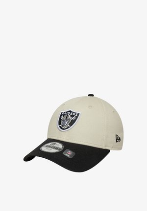 La casquette présente une couronne beige avec une visière noire. Elle a un logo brodé des Raiders sur le devant et une étiquette sur le bord indiquant la taille et la marque.