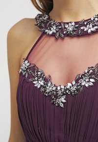 Lila klänning med plisserad bodice, genomskinlig halsringning och intrikata blomsterpärl- och kristalldekorationer runt kragen och bröstet.