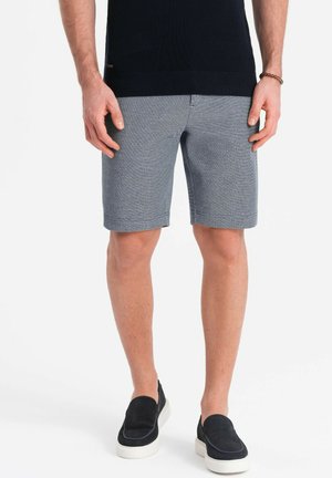 Shorts da uomo a quadri in cotone blu e grigio. Lunghezza fino alla coscia, progettati con tasche frontali. Abbinati a scarpe scure senza lacci.