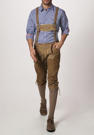 Mann trägt traditionelle braune Lederhose mit bestickten Hosenträgern, einem blau karierten Hemd, knielangen Socken und braunen Schuhen.