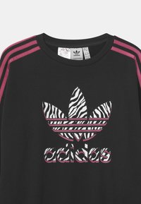 Sweat-shirt Adidas noir avec des accents d'épaules à rayures roses, un logo feuille à motif zèbre et le lettrage blanc audacieux "adidas".