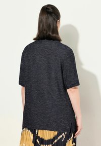 Granatowa bluzka z krótkim rękawem o teksturowanym wzorze i bocznymi rozcięciami, noszona na plisowanej, wielokolorowej spódnicy.