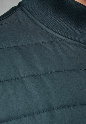 Dunkelgrüner gesteppter Stoff mit einem gerippten Kragen, der diagonale Steppmuster und eine glatte Textur aufweist.