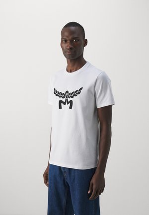 Weißes Baumwoll-T-Shirt mit einem schwarzen Grafikdesign von Flügeln und Initialen auf der Vorderseite. Kurze Ärmel und Rundhalsausschnitt.