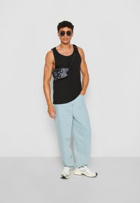 Black sleeveless tank top, light blue oversized jeans, black patterned crossbody bag, silver sneakers, and black sunglasses.