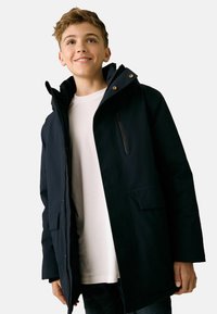 Giacca impermeabile blu navy con cappuccio, chiusura con zip, tasca sul petto e tasche laterali. Tessuto liscio con vestibilità strutturata.